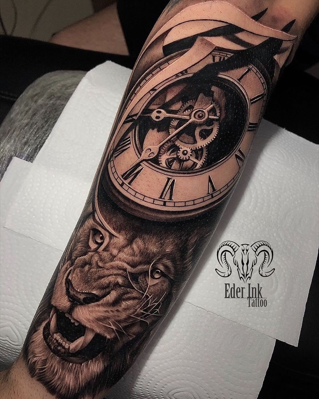 10adeya08lwgbpp7l6qgzfg Tatuagem de leão realista com relógio de engrenagens no braço, em tons de preto e cinza.