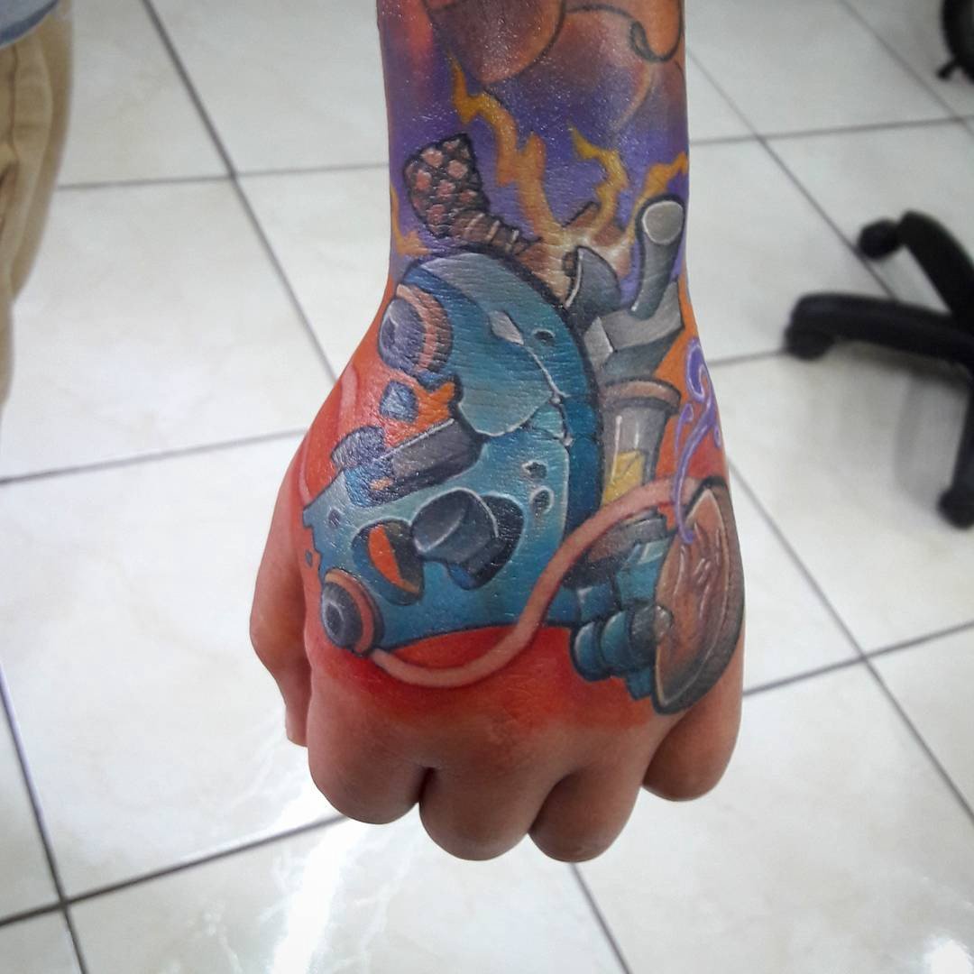 142ktimrty90d5aln8yjxda-1 Tatuagem colorida de design mecânico e abstrato na mão de uma pessoa.