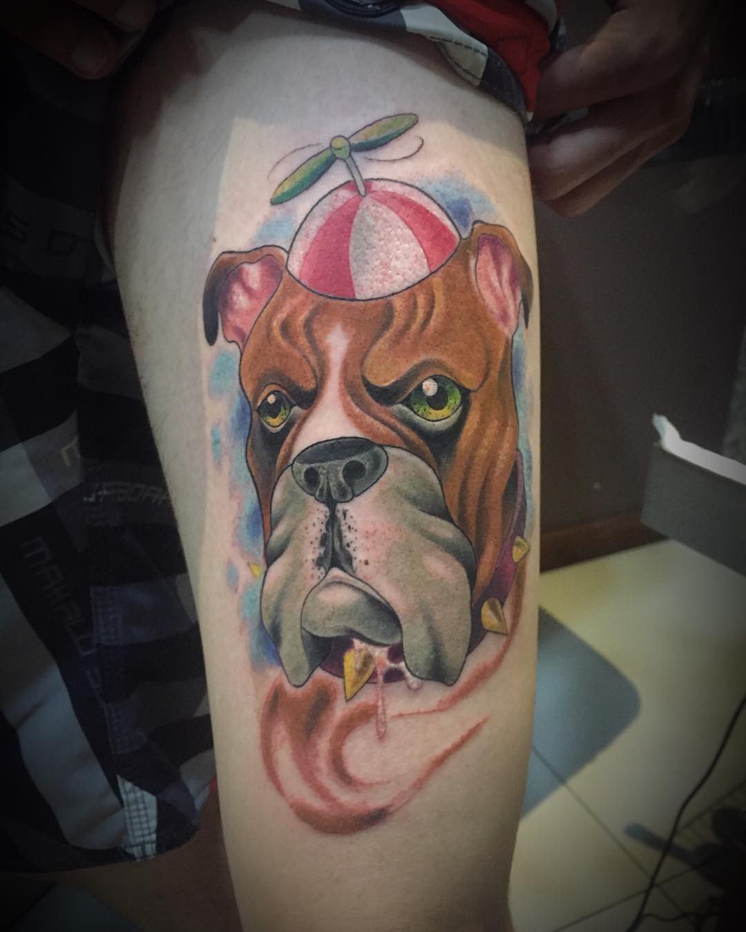 16jxewmtuijaplqieywklnw-1 Uma tatuagem colorida de um cachorro com chapéu de hélice em uma perna.