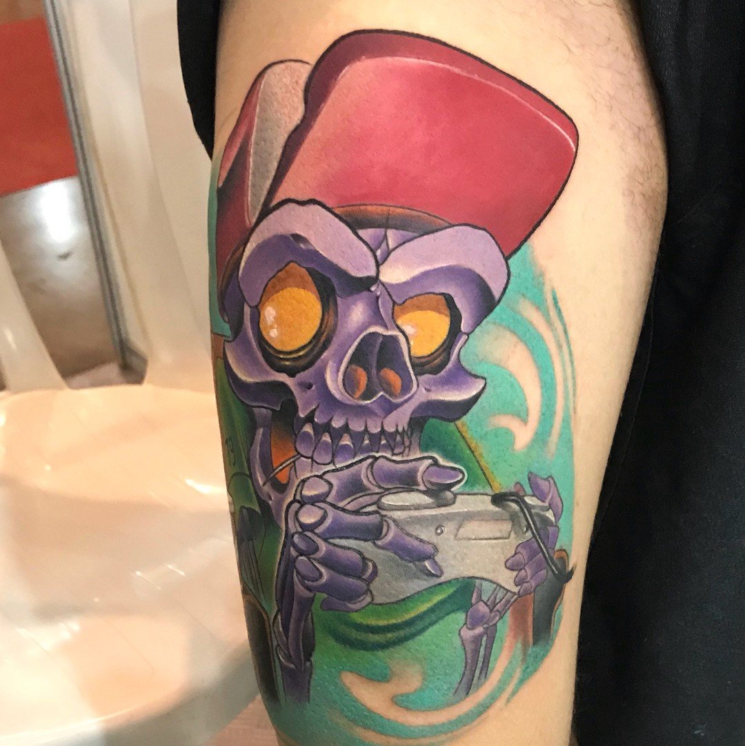 16l-c3-grtltwqglz3tel2q-1 Uma tatuagem colorida de esqueleto segurando um controle de videogame, com cores vibrantes e detalhes expressivos.