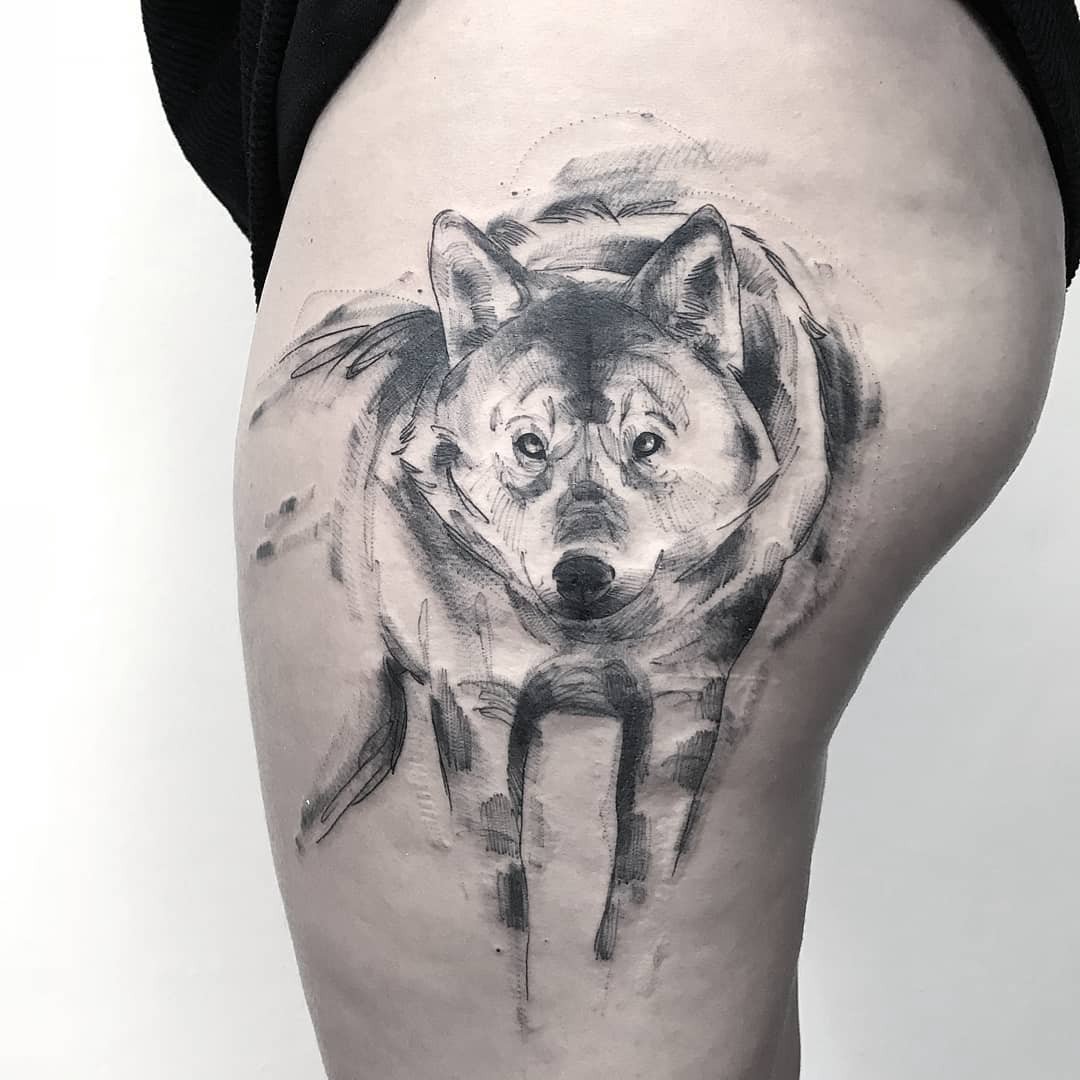 Tatuagem de um lobo em estilo aquarela no braço de uma pessoa, com traços escuros e sombreados.
