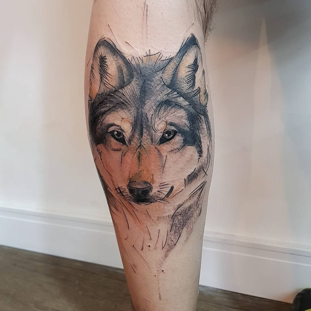 Tatuagem de lobo realista em uma perna, com detalhes em tons de cinza e marrom.