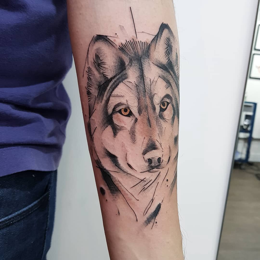 Tatuagem de lobo em estilo geométrico no antebraço de uma pessoa, com detalhes em preto e cinza.