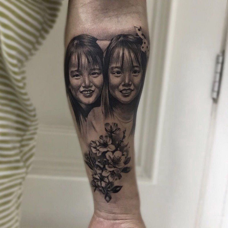 1djtsxjqzyaeg9h_cgoiieq-1 Desenho de tatuagem no braço com rostos de duas crianças e flores abaixo.