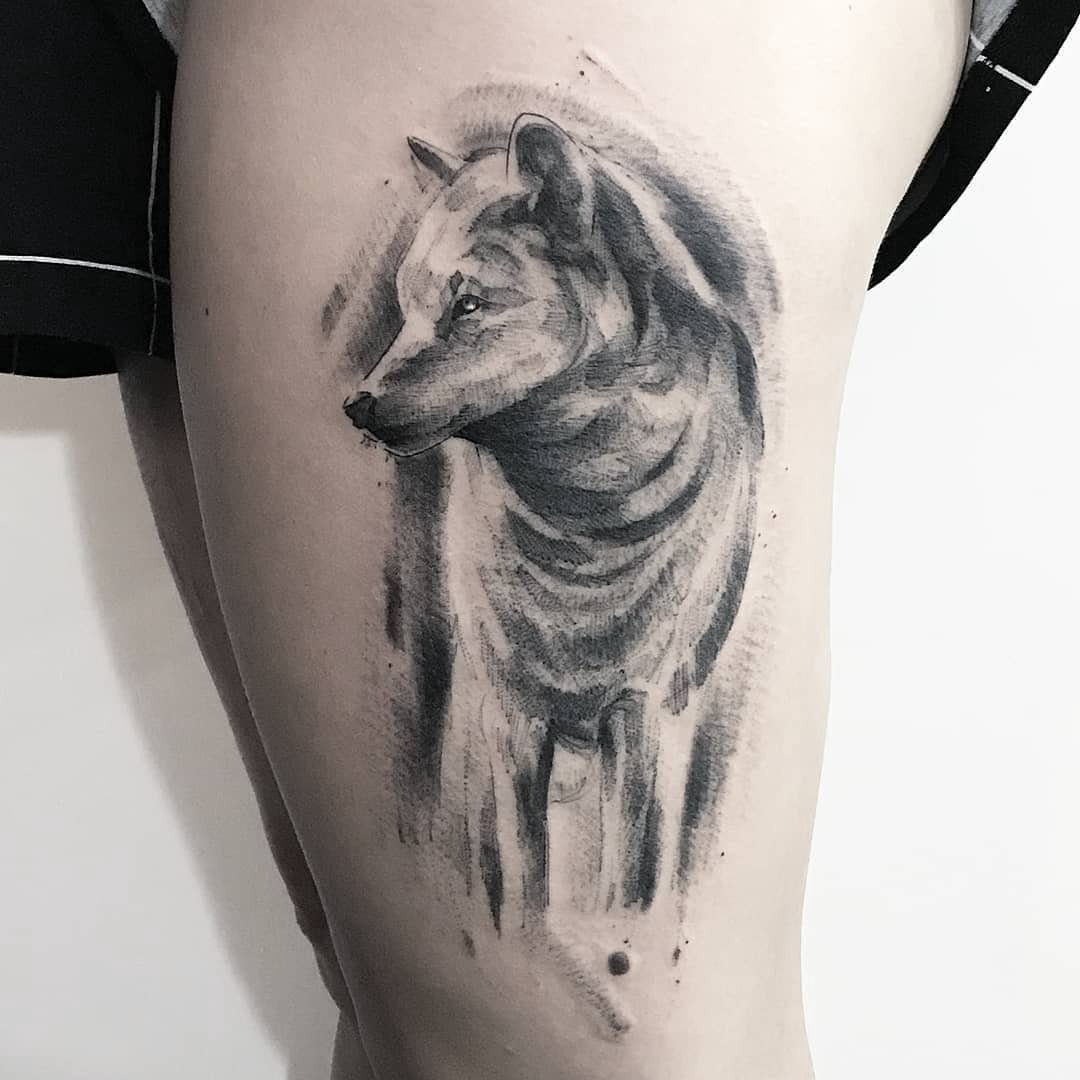 Uma tatuagem de lobo em estilo aquarela no braço de uma pessoa.