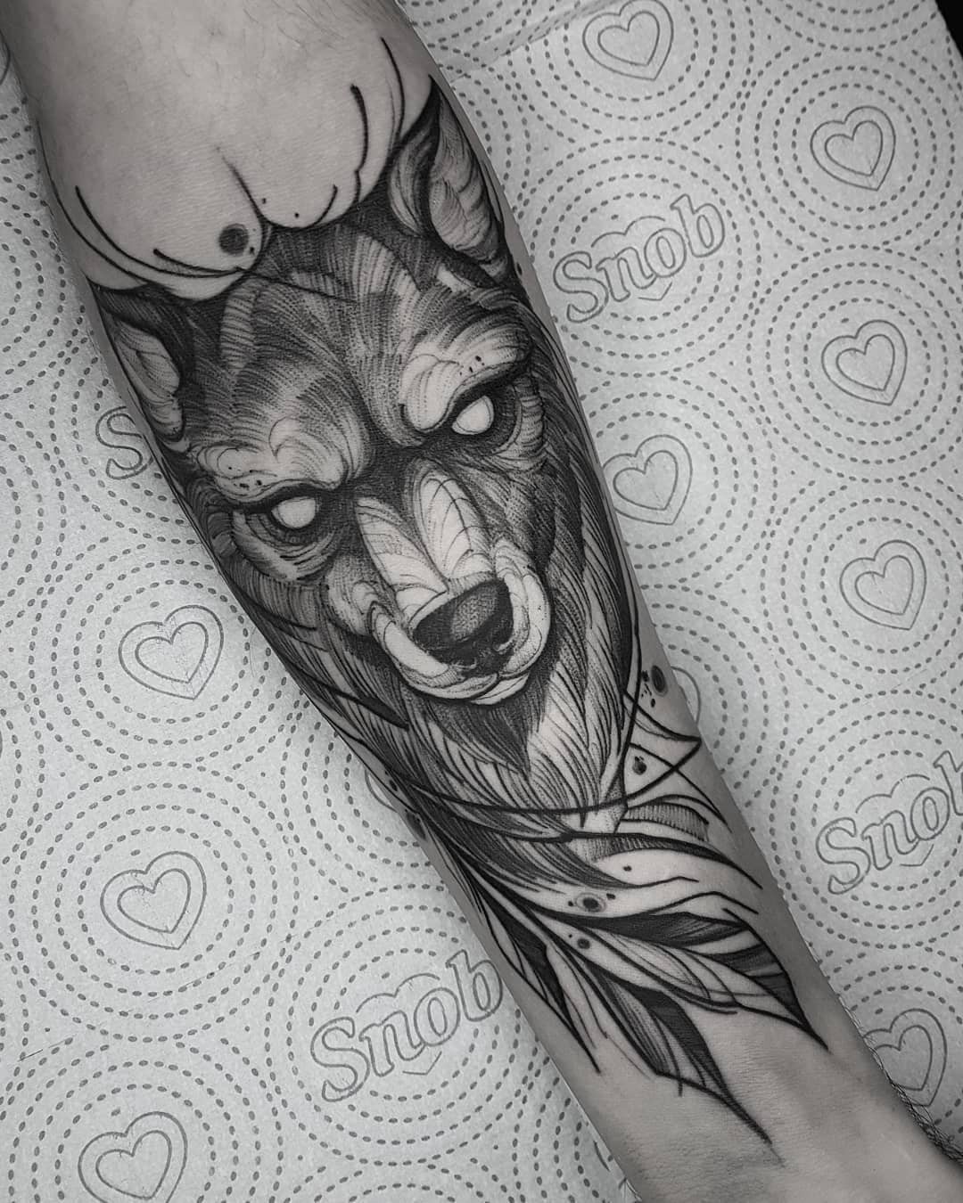 Tatuagem em preto e cinza de um lobo com detalhes geométricos no antebraço de uma pessoa.