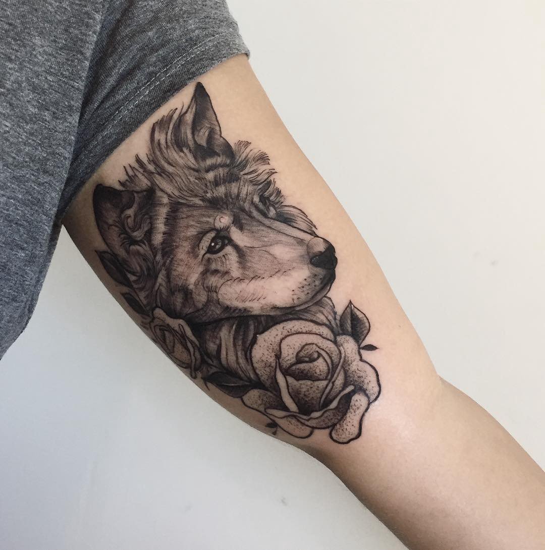 Tatuagem de lobo com rosas no braço de uma pessoa, em estilo preto e cinza.