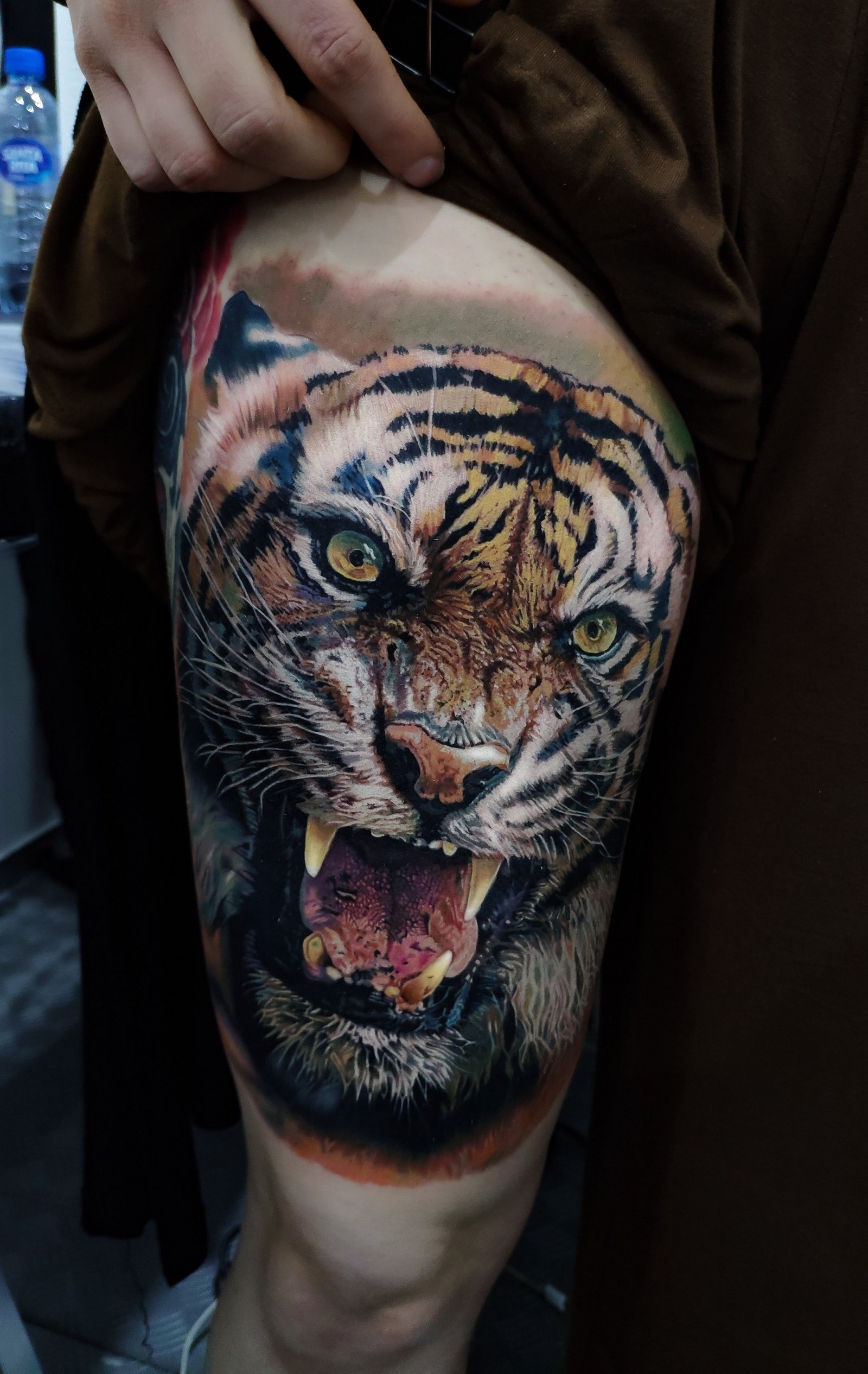 1i_ei5dkz0e_igt2mtjl9pw-1 Tatuagem realista de tigre rugindo na perna de uma pessoa, com detalhes vibrantes e expressivos.