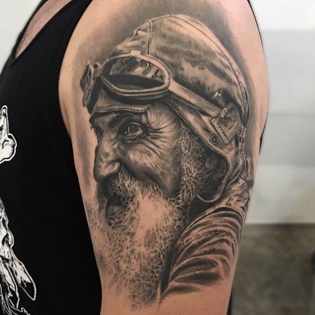 1j1axxrwdngz6fhsifr7-bq-1 Uma tatuagem de um rosto envelhecido com chapéu e óculos, no braço de uma pessoa.