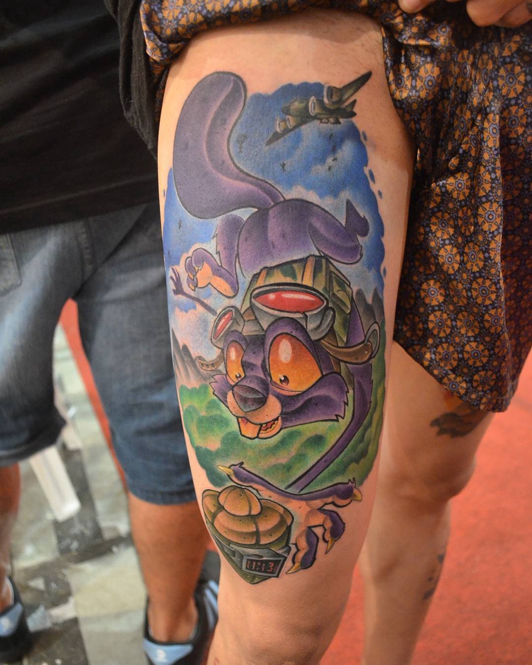 1jawojx1gi1eamfwyzq-_qq-1 Pessoa exibe uma tatuagem colorida de personagem animado com capacete, voando sobre paisagem com avião no céu.