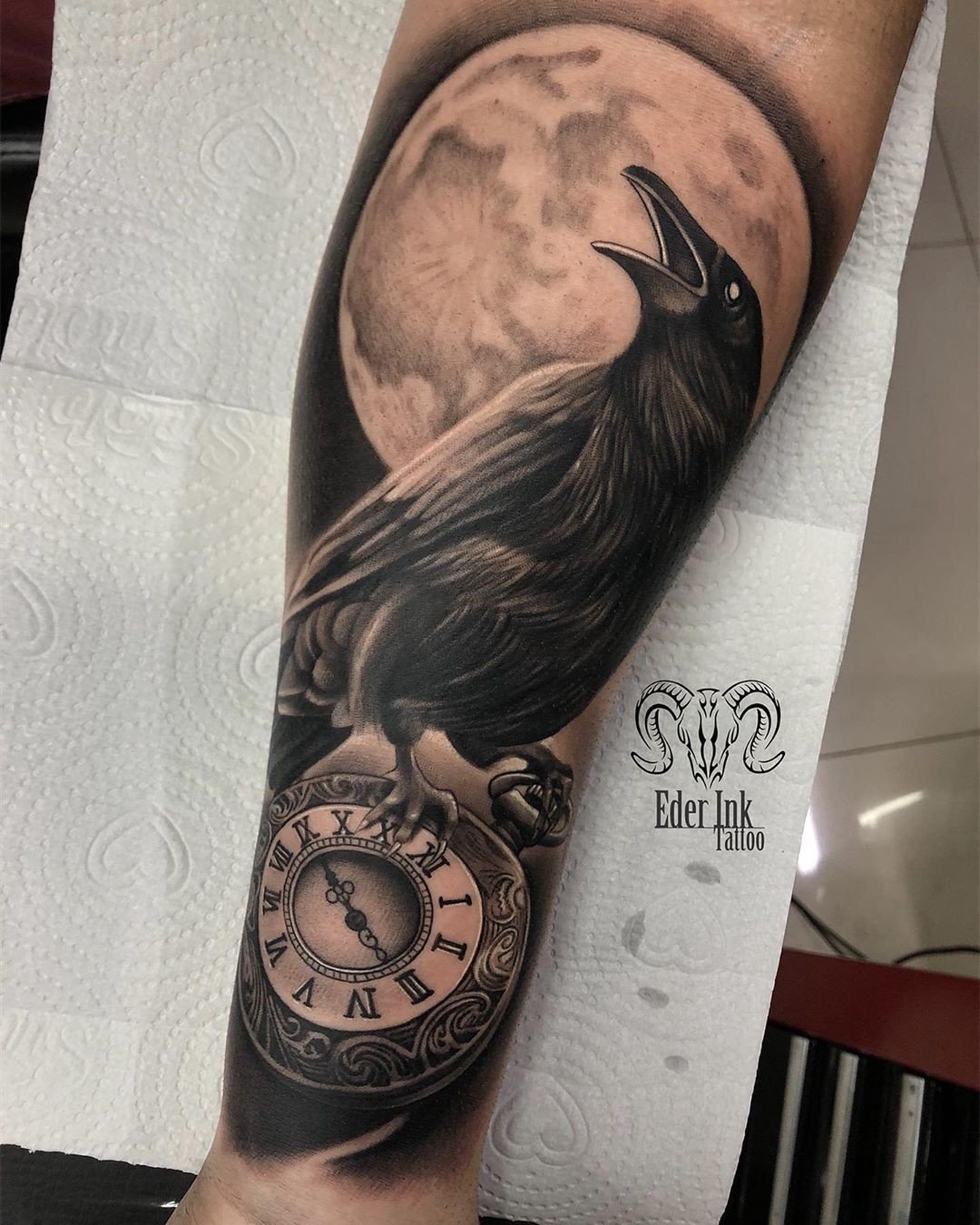 1o0fgzqesj4cfqppsctsggq Tatuagem de corvo sobre um relógio de bolso, com uma lua cheia ao fundo, em um braço humano.