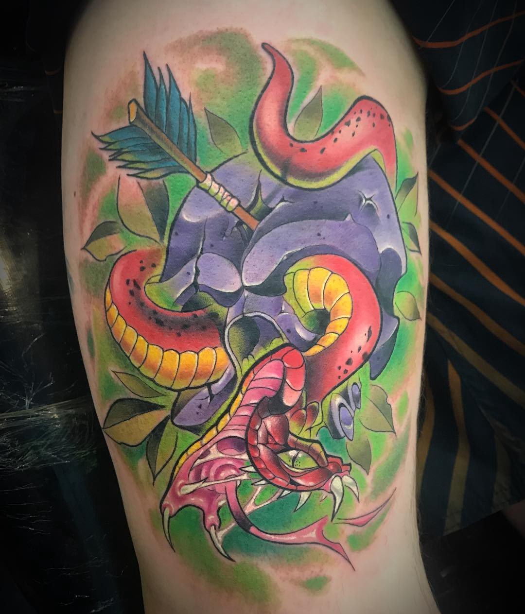 1pkeb6bjohvn-eikfzo6eea-1 Tatuagem colorida com caveira, serpente vermelha, flecha e folhas verdes.
