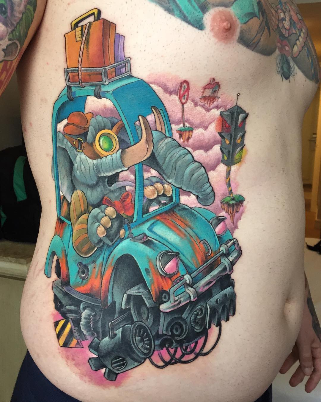 1raslleptkhfrxjz5uijtva-1 Um tatuagem colorida de um elefante dirigindo um carro azul com bagagem no teto, em um cenário de fantasia.