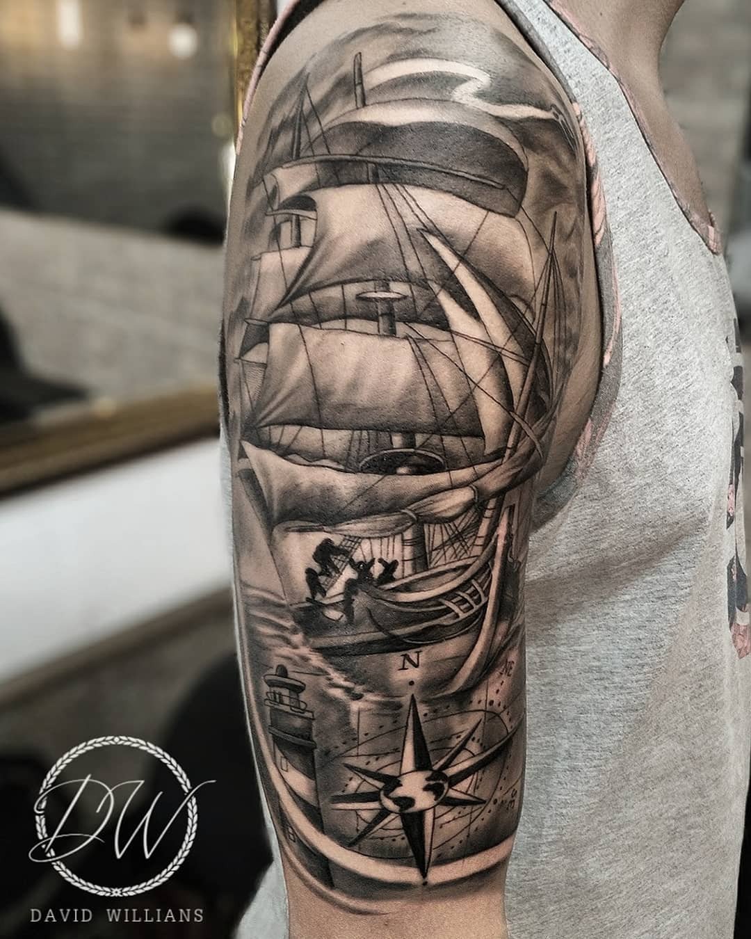 1rgd4rkdc7mx0ewalhovvrg Tatuagem em preto e cinza no braço, exibindo um navio à vela, bússola e farol detalhados.