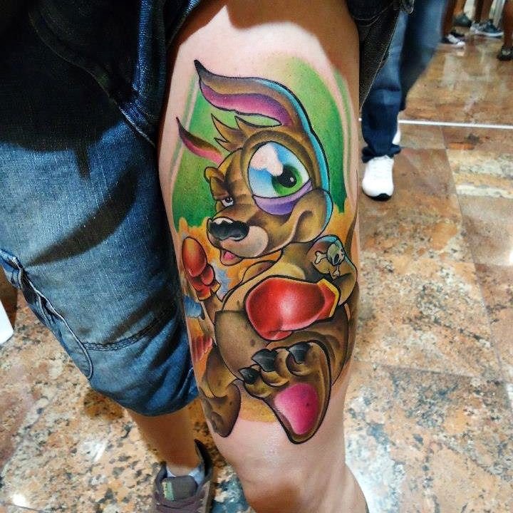1riibay5jco3dtpzakqcywa-1 Tatuagem colorida de canguru com luvas de boxe no braço de uma pessoa, com fundo verde e detalhes em vermelho.