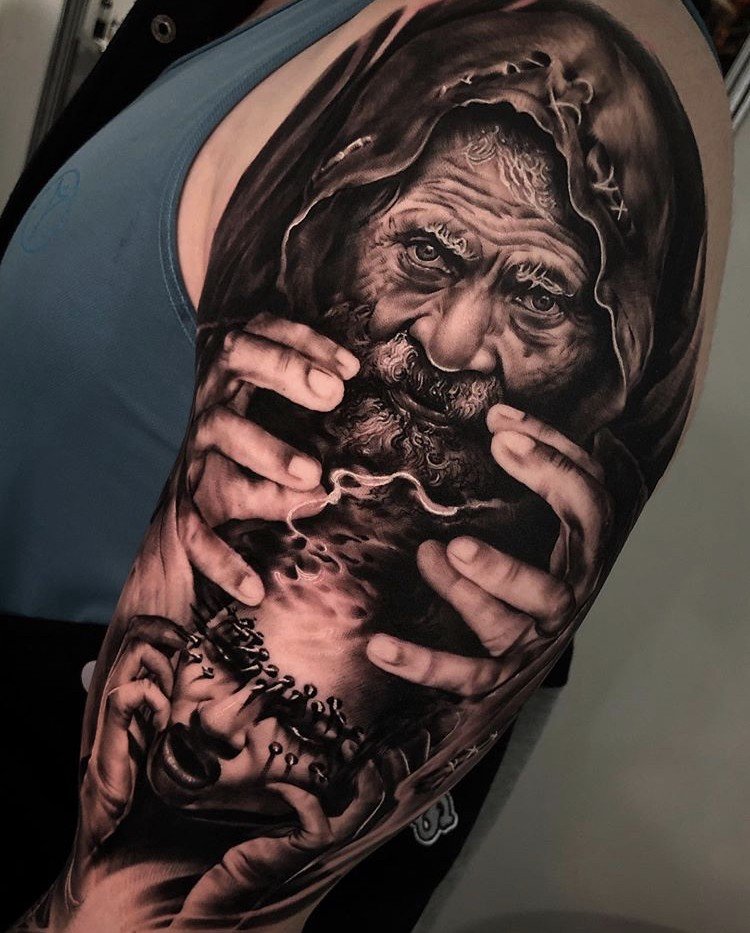 1u4ppj0tisogwfmbz245pja-1 Tatuagem realista de um homem com capuz, segurando um rosto em suas mãos, em um braço.