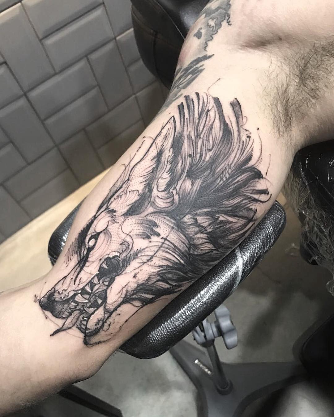 Braço com tatuagem de lobo estilizado em preto, mostrando detalhes do pelo e da expressão do animal.