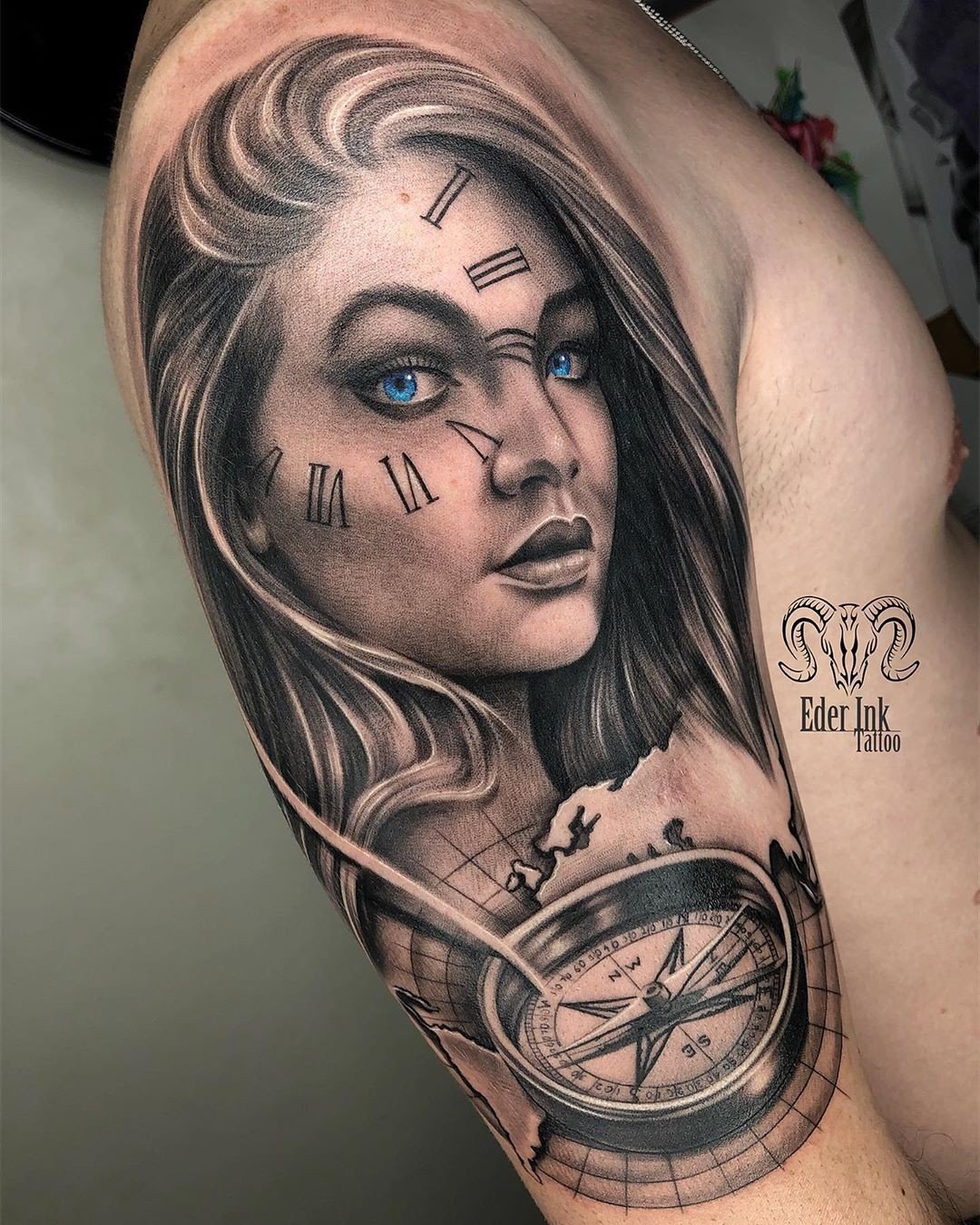 1volv1qvxhw-yka9pyu4msa Tatuagem de rosto feminino com olhos azuis, números romanos e uma bússola sobre um mapa no braço de uma pessoa.
