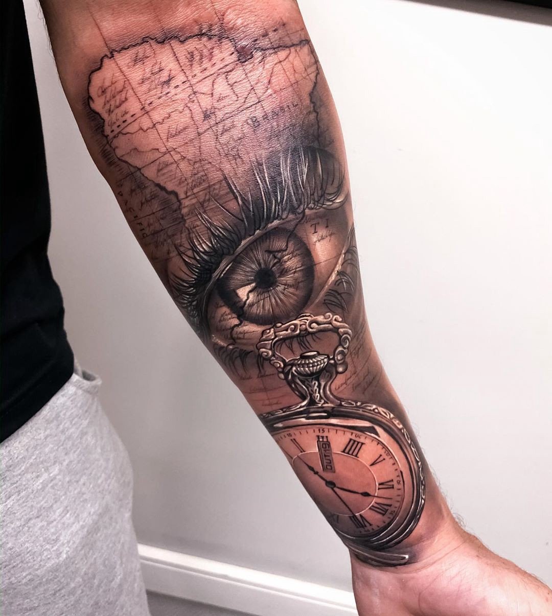 1x8ypvrk7lzppaegvlvji9a Um braço tatuado com um olho, mapa e relógio de bolso, exibindo detalhes realistas e sombreados.