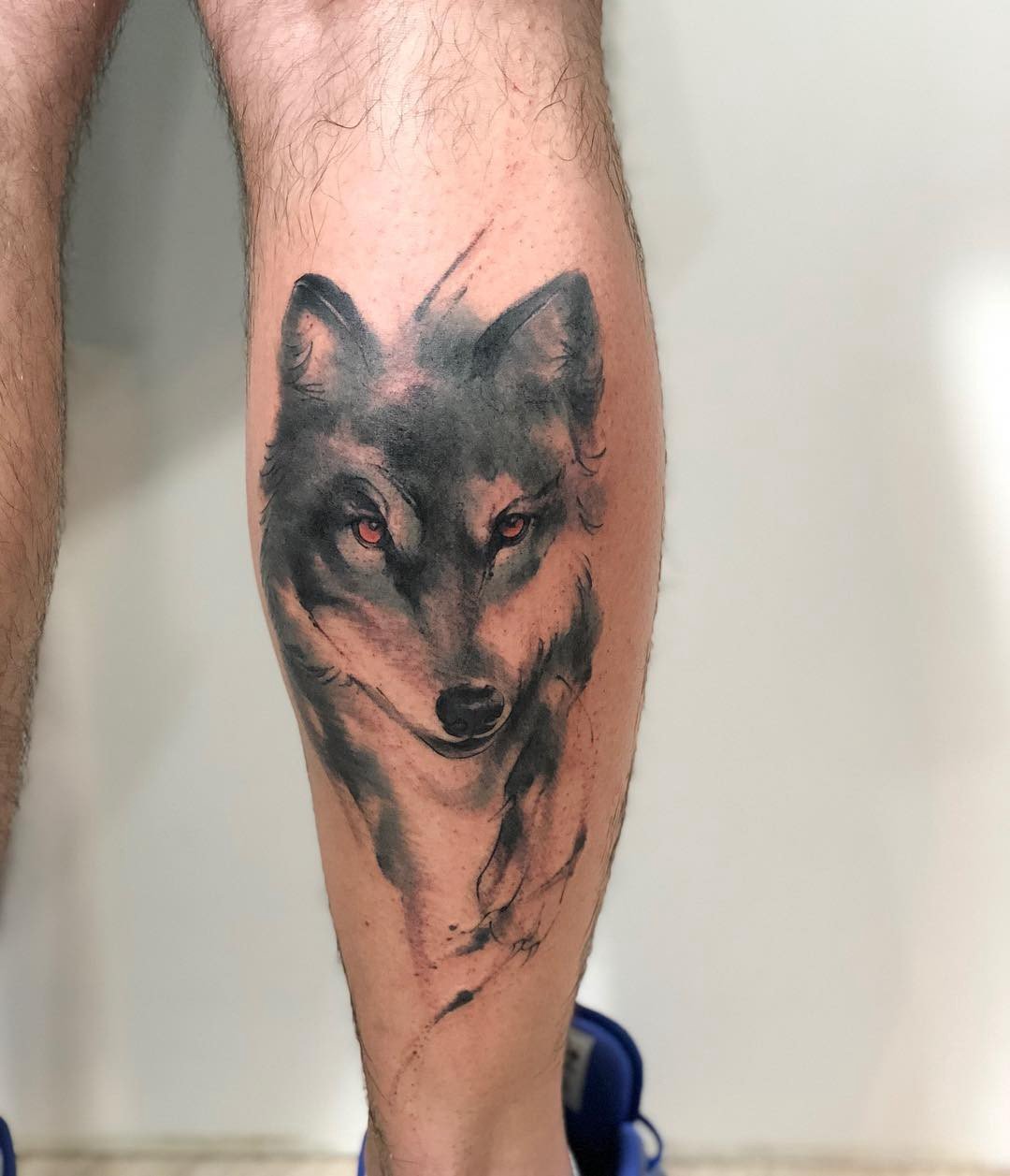 Perna com tatuagem realista de lobo cinza, olhando para frente, com detalhes sombreados.