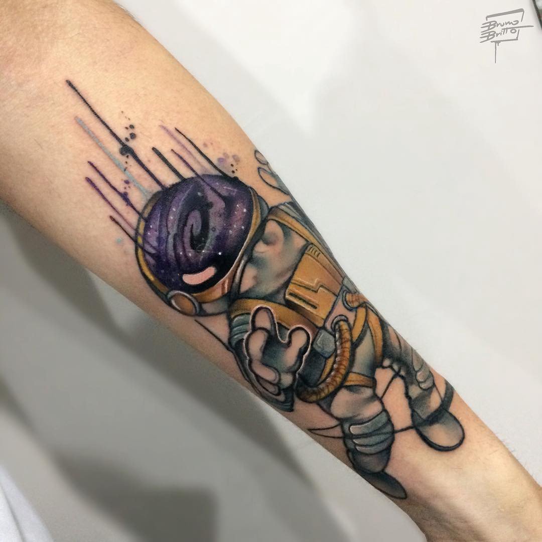 1xmtxp5-f-z_mwj_lgmwpca-1 Tatuagem colorida de astronauta com capacete galáctico no antebraço de uma pessoa.