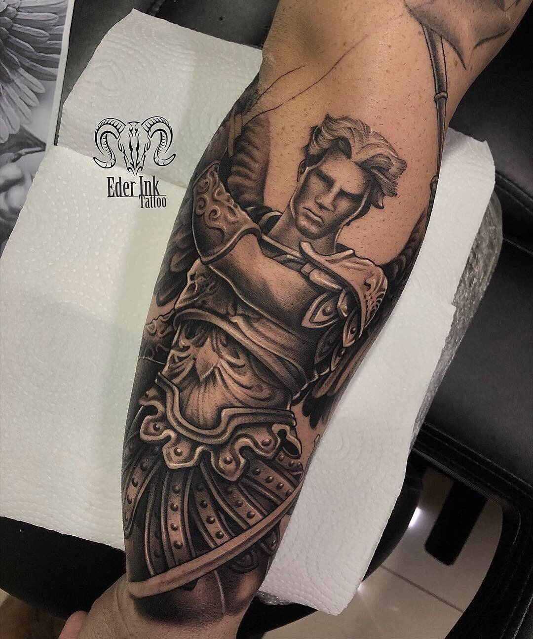1zj6snp7gtdwcu3lcgnv-ka Tatuagem detalhada de guerreiro com armadura no braço de uma pessoa, sobre papel toalha.