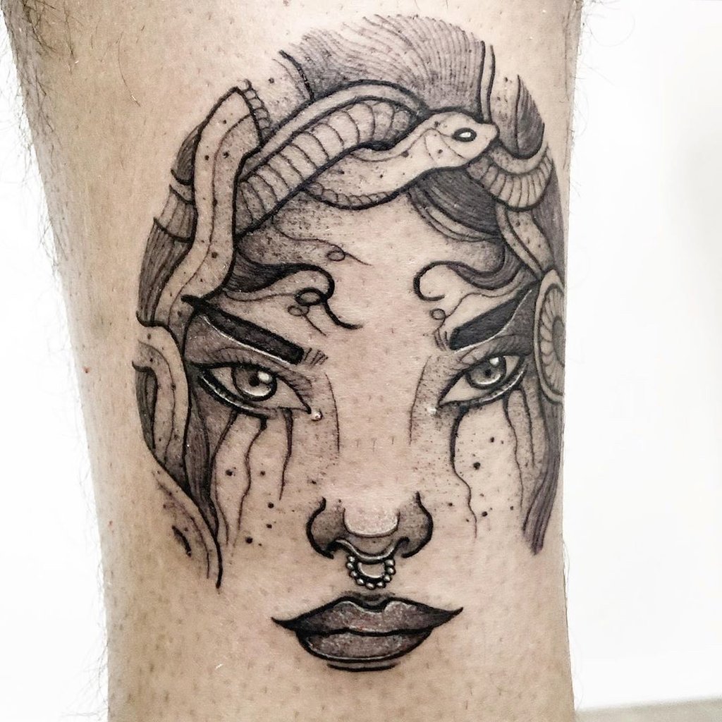 w1024-149 Tatuagem em preto e branco de um rosto com serpentes no cabelo e piercing no nariz.