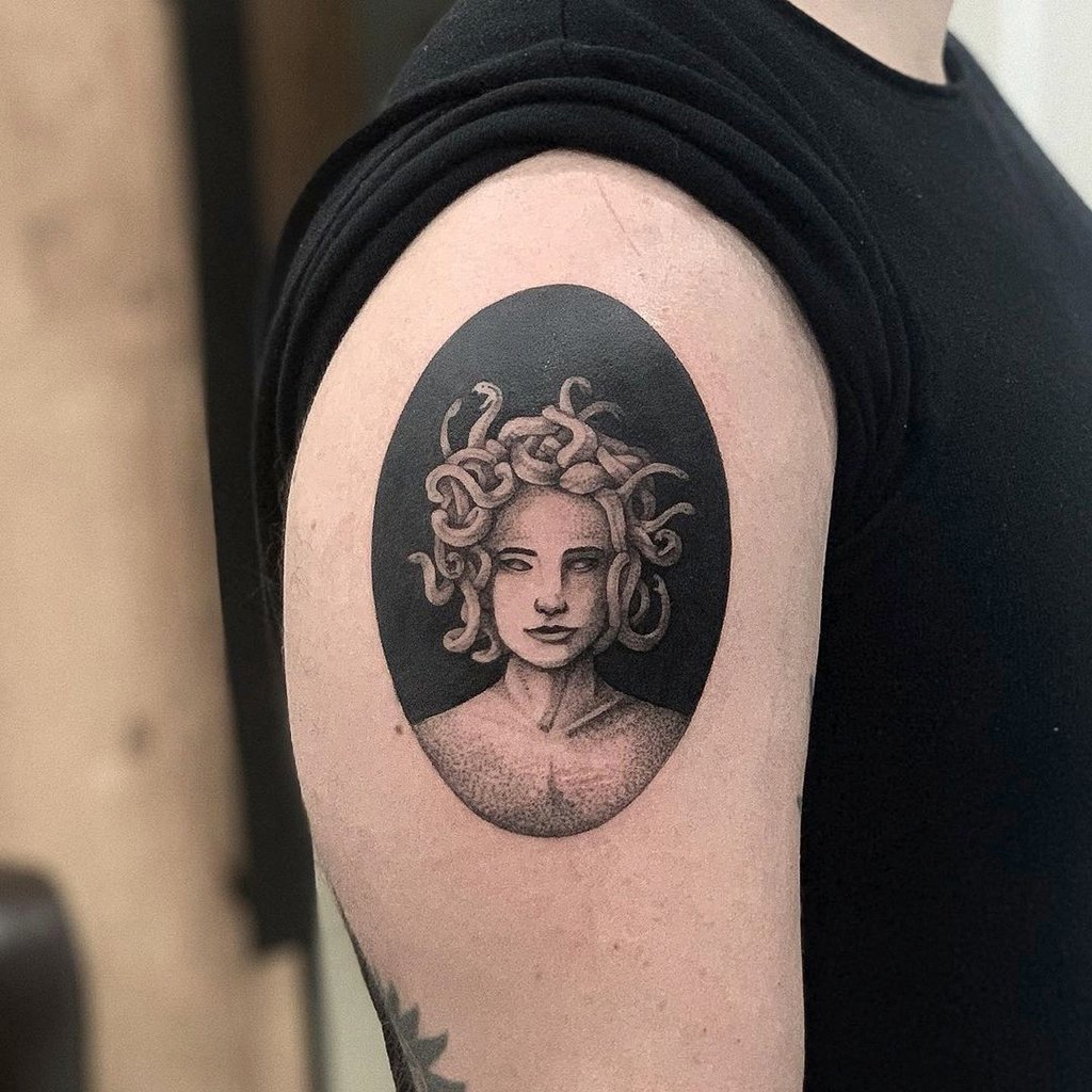 w1024-159 Tatuagem no braço de uma figura com cabelos de serpente dentro de um oval preto, em estilo monocromático.