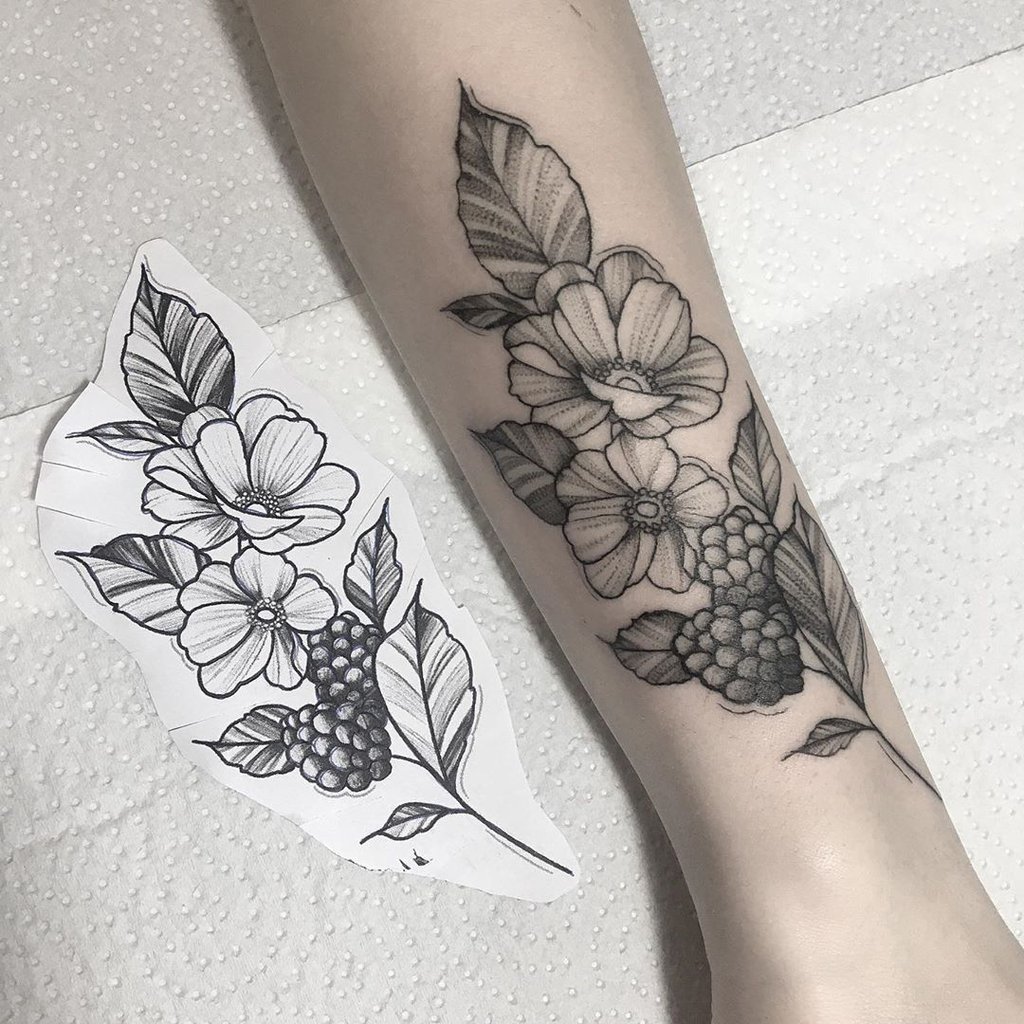 w1024-18 Braço com tatuagem de flores e folhas, ao lado de desenho similar em papel.