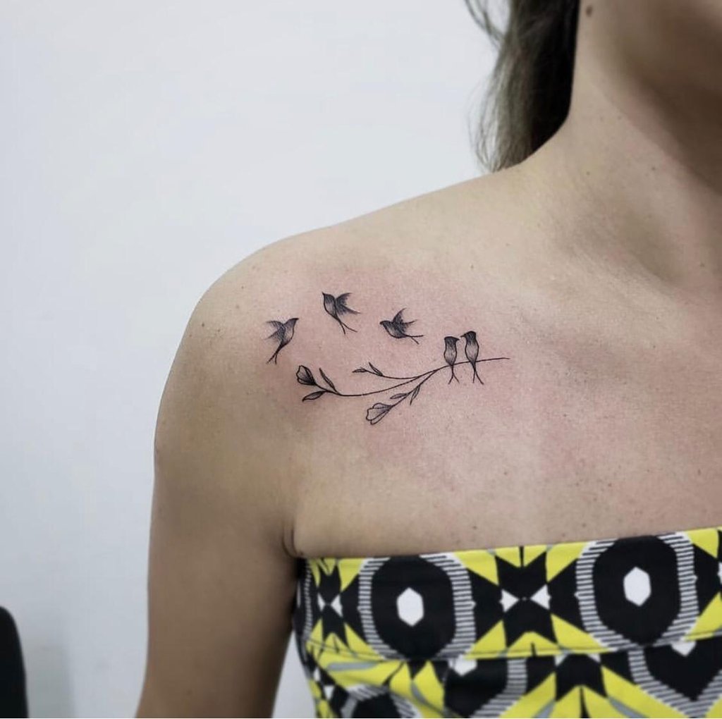Tatuagem delicada no ombro com pássaros em um galho, simbolizando liberdade e conexão com a natureza.