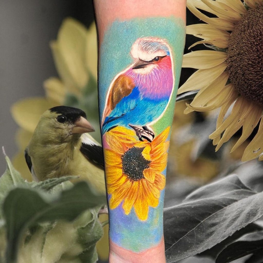 Ideias de Tatuagens Femininas no Pescoço 2 Tatuagem colorida de pássaro exótico pousado em um girassol, com um pássaro real em segundo plano.