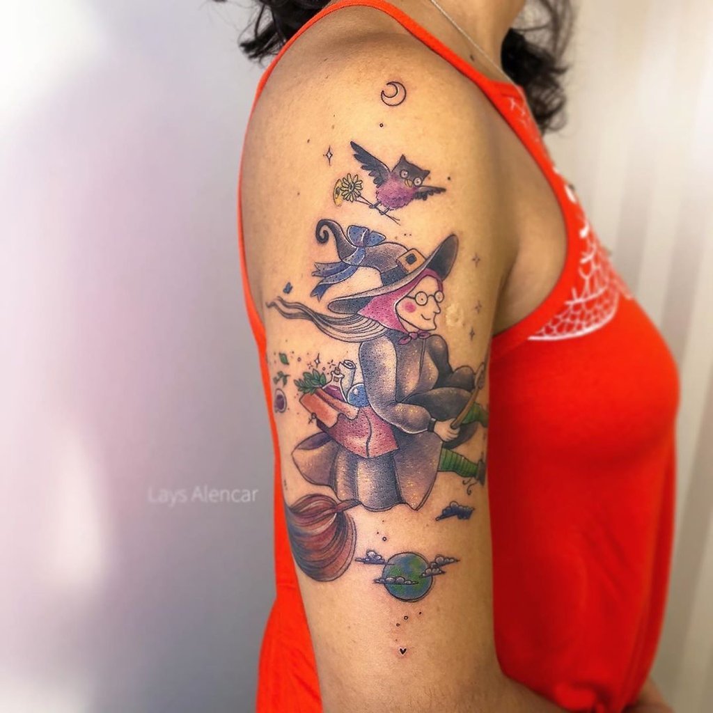 w1024-38 Tatuagem no braço de uma pessoa, retratando uma bruxa voando em uma vassoura com um gato e um planeta.