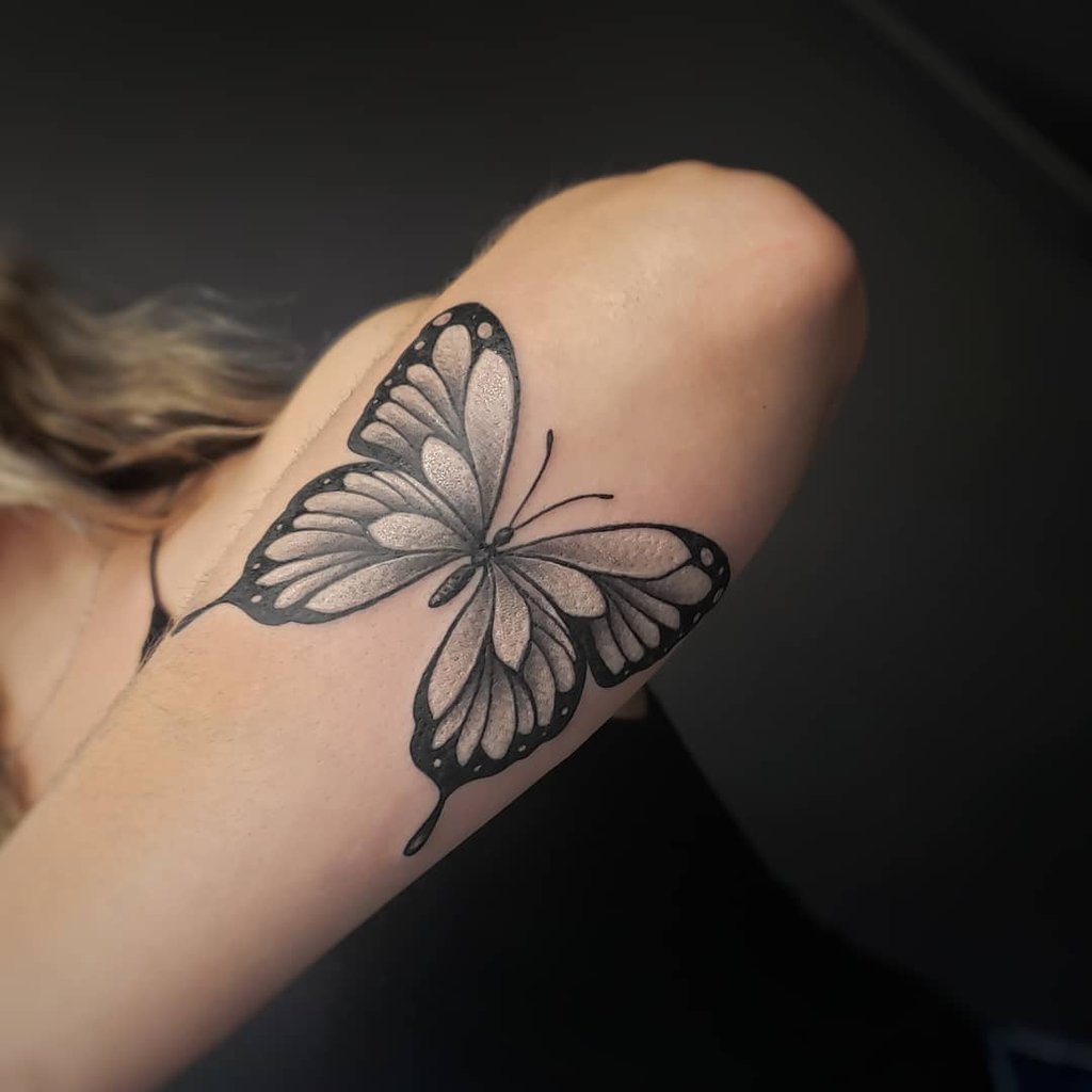 w1024-46 Um braço com uma tatuagem de borboleta preta e cinza, exibindo detalhes nas asas.