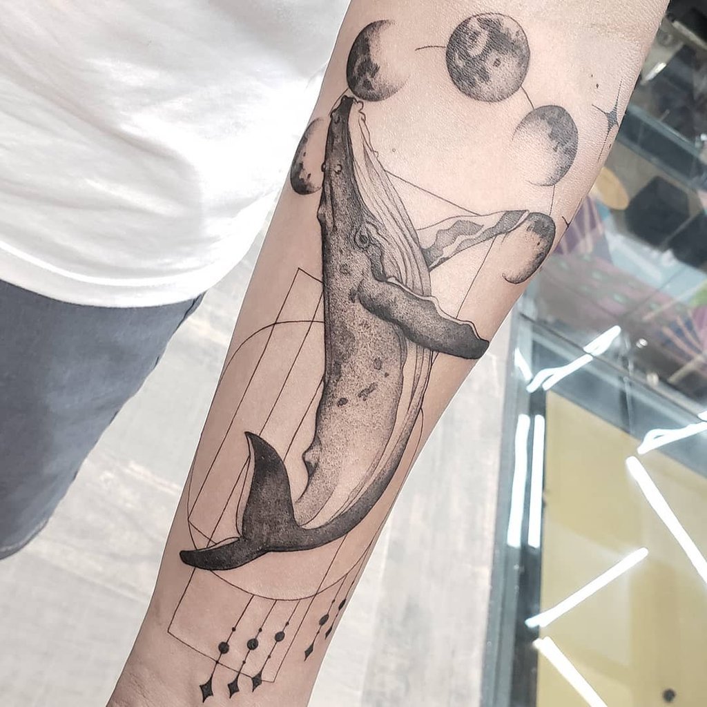 w1024-51 Tatuagem de baleia no braço com elementos geométricos e fases da lua ao fundo.