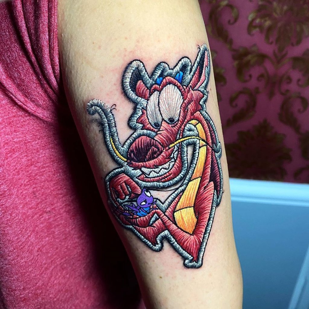 w1024-53 Tatuagem de dragão estilizado em braço, com efeito de bordado e detalhes coloridos.