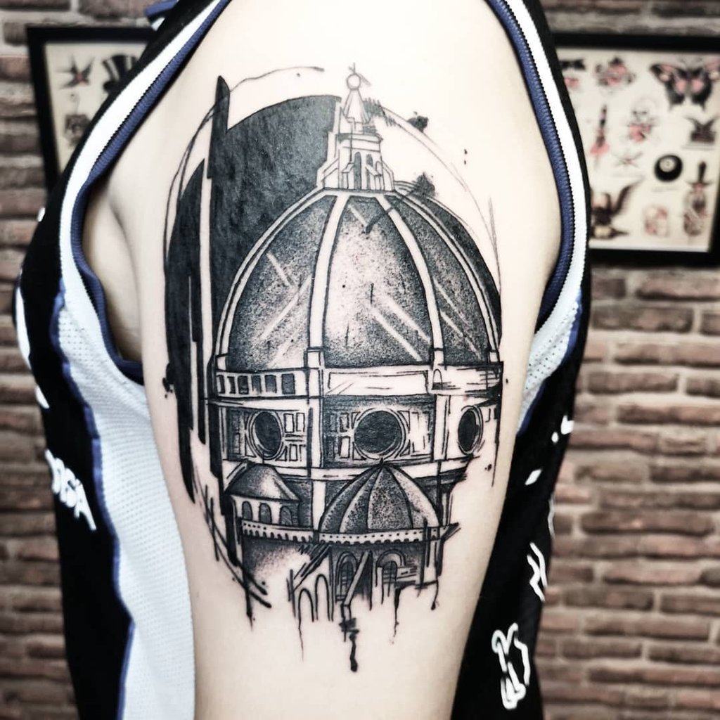 w1024-59 Braço com tatuagem detalhada de uma cúpula arquitetônica, em estilo preto e branco, ao fundo parede de tijolos.