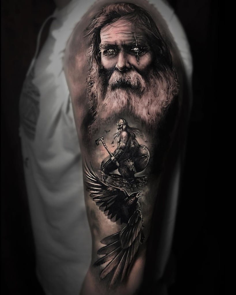 w819-31 Braço tatuado com rosto de homem idoso, guerreiro com machado e corvo voando, em estilo realista.