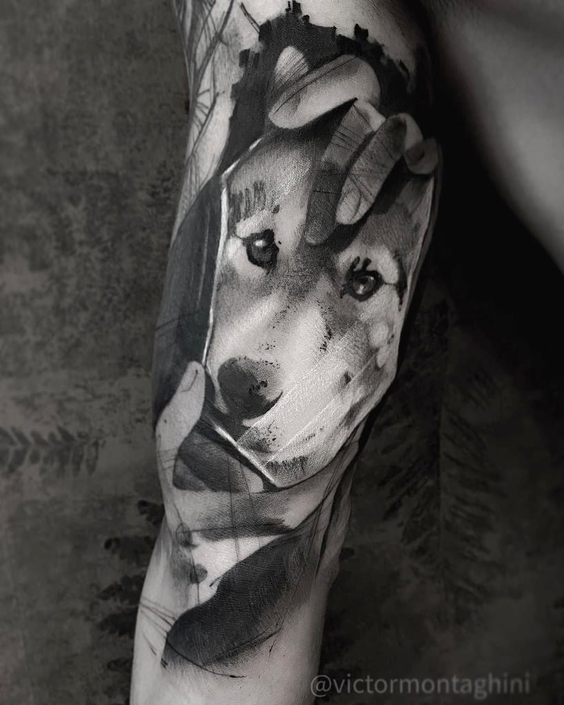 Tatuagem em preto e branco de um cachorro sendo acariciado por mãos, com fundo abstrato.