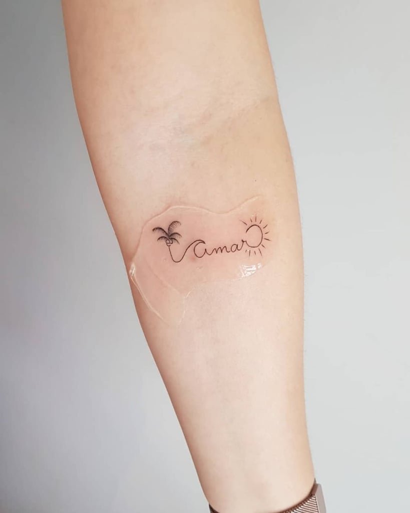 w819-325 Braço com uma tatuagem da palavra "Amar", acompanhada de um desenho de palmeira e sol.