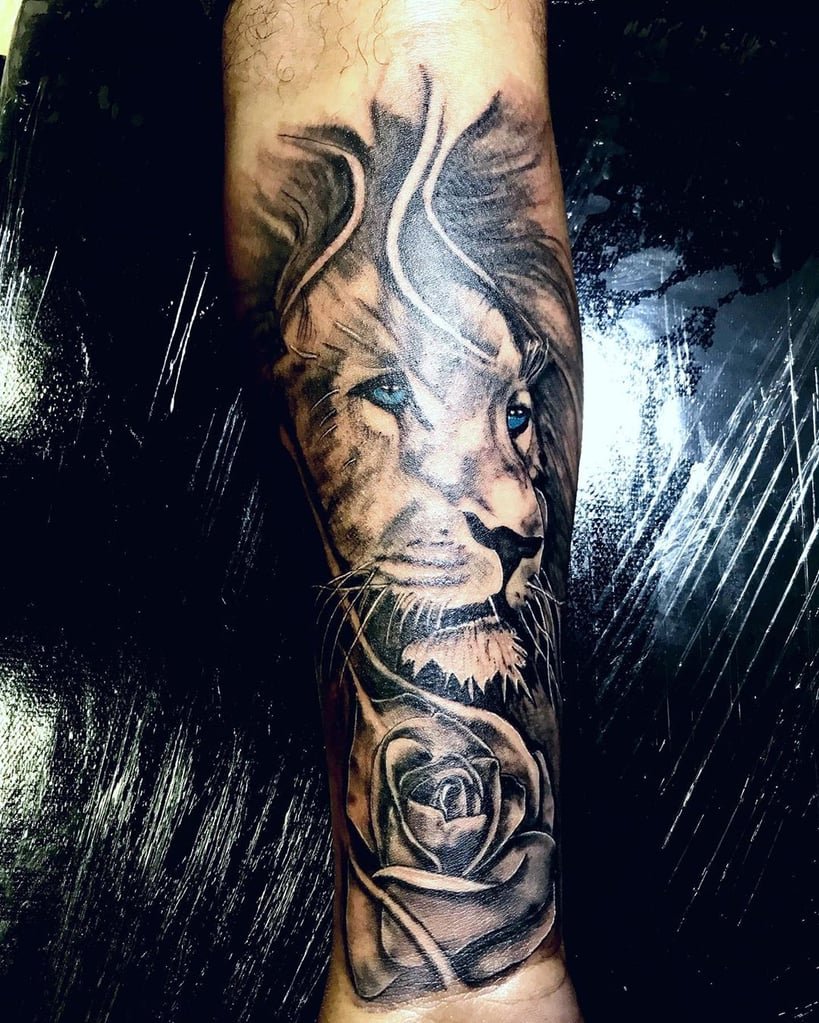 w819-43 Uma tatuagem no braço com um leão de olhos azuis e uma rosa na parte inferior.