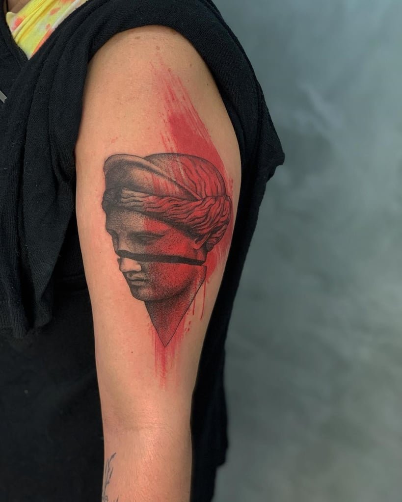 w819-8 Tatuagem no braço de um busto clássico com detalhes em vermelho e uma faixa preta nos olhos.