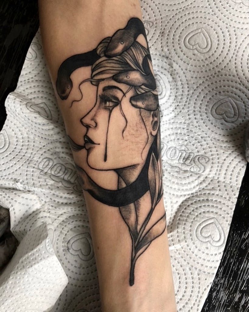 w819-97 Uma tatuagem no braço representa um rosto feminino com cobras em volta da cabeça, em estilo de arte sombria.