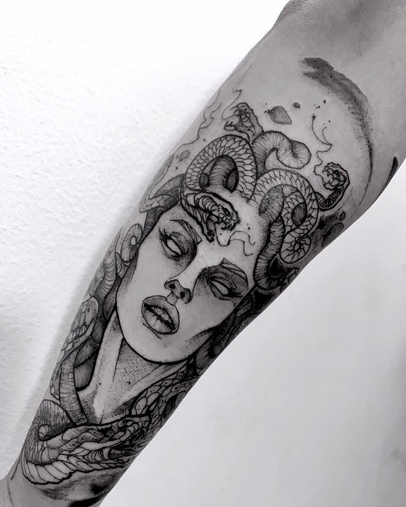 w820-4 Tatuagem em preto e cinza no braço, retratando um rosto feminino com cobras entrelaçadas ao redor da cabeça.