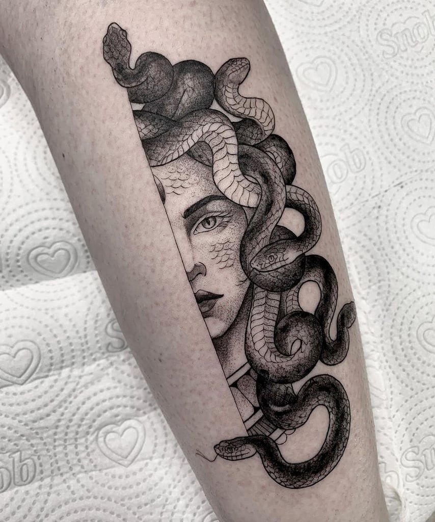 w854 Tatuagem em preto e branco de uma figura mitológica com cobras no cabelo, feita na perna de uma pessoa.