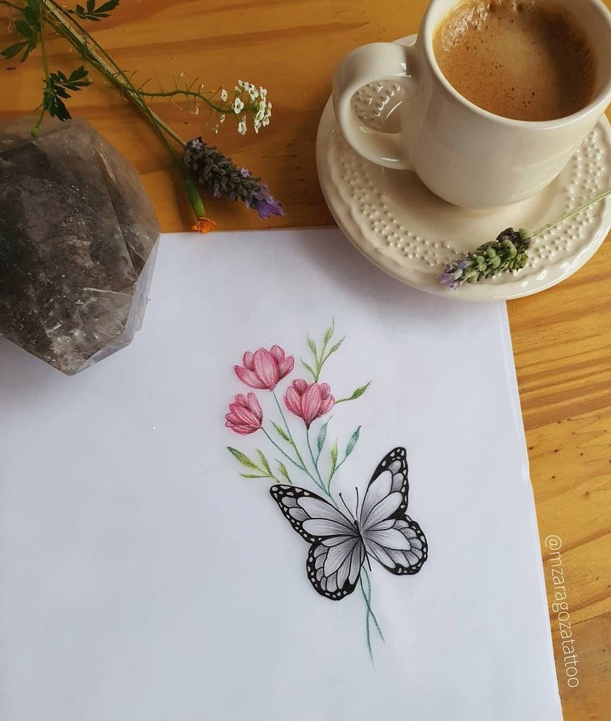 w868-2 Desenho de borboleta e flores em papel, próximo a uma xícara de café, flores e um cristal sobre a mesa.