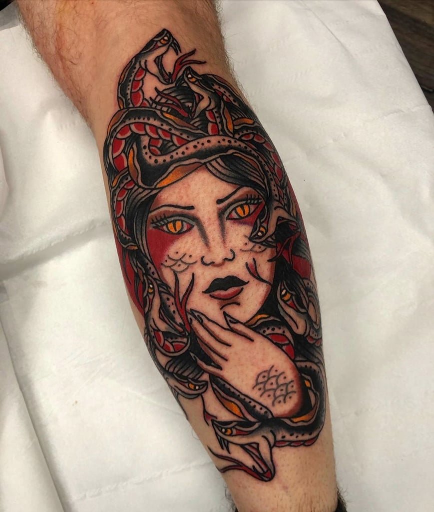 w869 Tatuagem colorida de uma figura mitológica com cobras na cabeça e olhos amarelos, aplicada na perna.