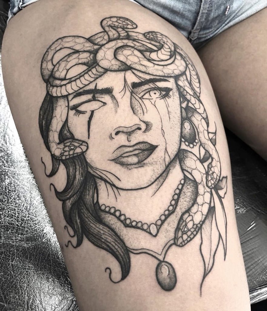 w881 Tatuagem de rosto feminino com cobras no cabelo, lágrimas e colar, localizada na perna de uma pessoa.