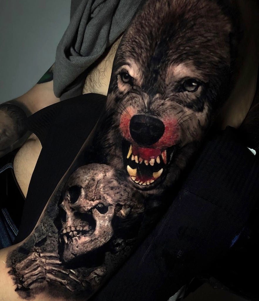 Desenho de um lobo feroz e um crânio em um braço tatuado.
