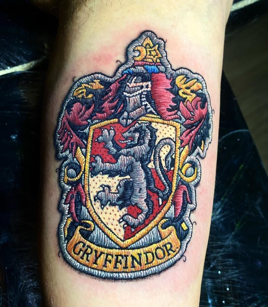w893 Tatuagem colorida de brasão com leão em destaque, exibindo detalhes em vermelho, amarelo e cinza.