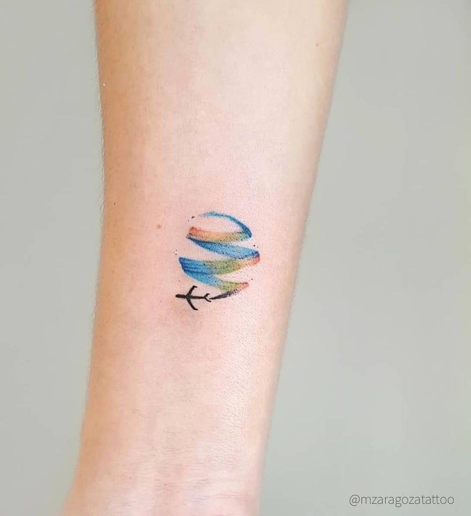 w933-1 Uma tatuagem colorida no braço representa um avião sobre um planeta estilizado com listras azuis e laranja.